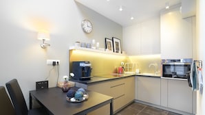 Een moderne keuken met een koffieapparaat, waterkoker en een klok aan de muur.