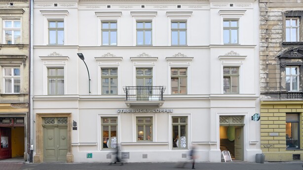 Een wit gebouw met een Starbucks Coffee bord, grote ramen en een balkon.