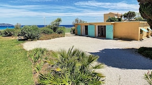 A coastal property with a gravel driveway, a small building with blue shutters, and a view of the sea.