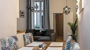 A modern living room with a sofa, a dining table with papers, and geometric pendant lights. - 3D WAWEL Apartament (Kraków)