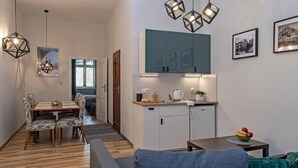 A modern living room with a sofa, a dining area with a table and chairs, a kitchen with cabinets and a countertop, and pendant lighting. - 3D WAWEL Apartament (Kraków)