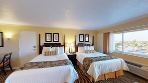 Quarto de hotel com duas camas, uma escrivaninha, uma cadeira e uma janela com vista para a cidade.
