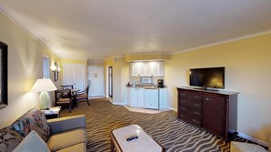 A hotel room with a living area, kitchenette, and a television.