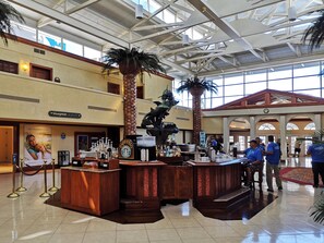 A spacious lobby with a high ceiling, a central bar area, and a large window providing natural light.