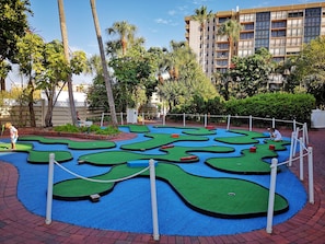A miniature golf course with a winding layout, surrounded by a brick pathway and palm trees.