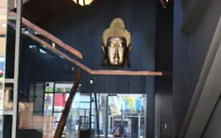 A wooden staircase with a glass railing, leading to a dark interior space with a large, ornate sculpture on the wall.