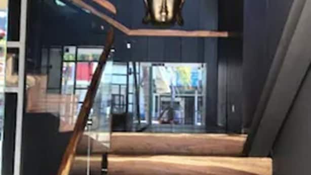 Una escalera de madera con barandilla de cristal que conduce a un espacio interior oscuro con una gran escultura ornamentada en la pared.