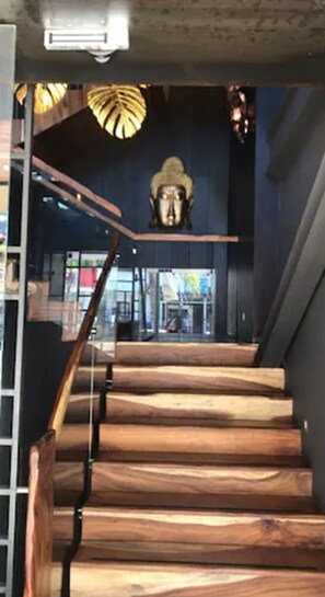 Una escalera de madera con barandilla de cristal que conduce a un espacio interior oscuro con una gran escultura ornamentada en la pared.