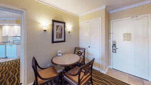 A hotel room with a dining area featuring a round table and four chairs, a framed picture on the wall, and a door with a lock and a key in the keyhole.