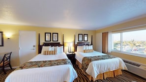A hotel room with two beds, a chair, a desk, and a large window offering a city view.