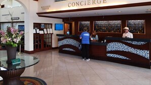A concierge desk with a sign above it, a reception area, and a glass table with a vase of flowers. - St Pete Beach | Couples Gulf Coast Retreat | Pool + Beach (St. Pete Beach)