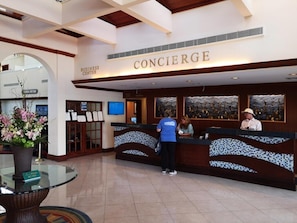 A concierge desk with a sign above it, a reception area, and a glass table with a vase of flowers. - St Pete Beach | Couples Gulf Coast Retreat | Pool + Beach (St. Pete Beach)