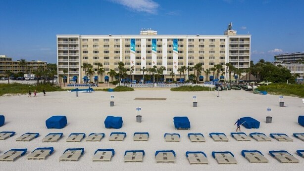 A hotel with a large building, a sandy beach in front, and rows of blue beach chairs.