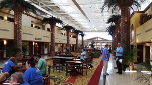 A spacious indoor area with high ceilings, palm trees, and a central walkway.