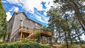 A two-story wooden house with a balcony, surrounded by trees and a natural landscape. - Amazing Location! Lakefront Waterside Deck (Chatham)