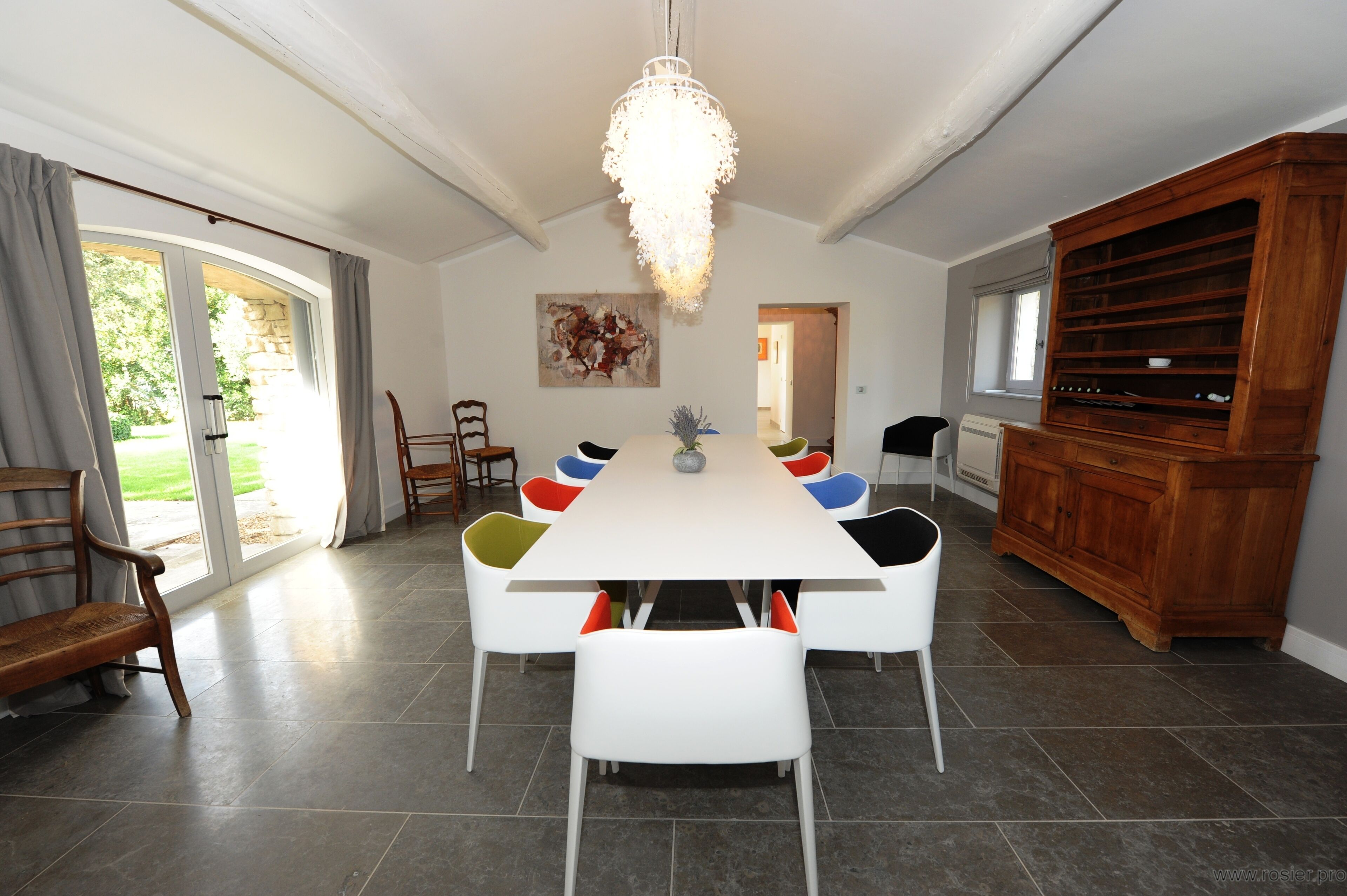 Ein Esszimmer mit einem langen Tisch, weißen Stühlen, einer Kristallleuchter und einem Holzkabinett.
