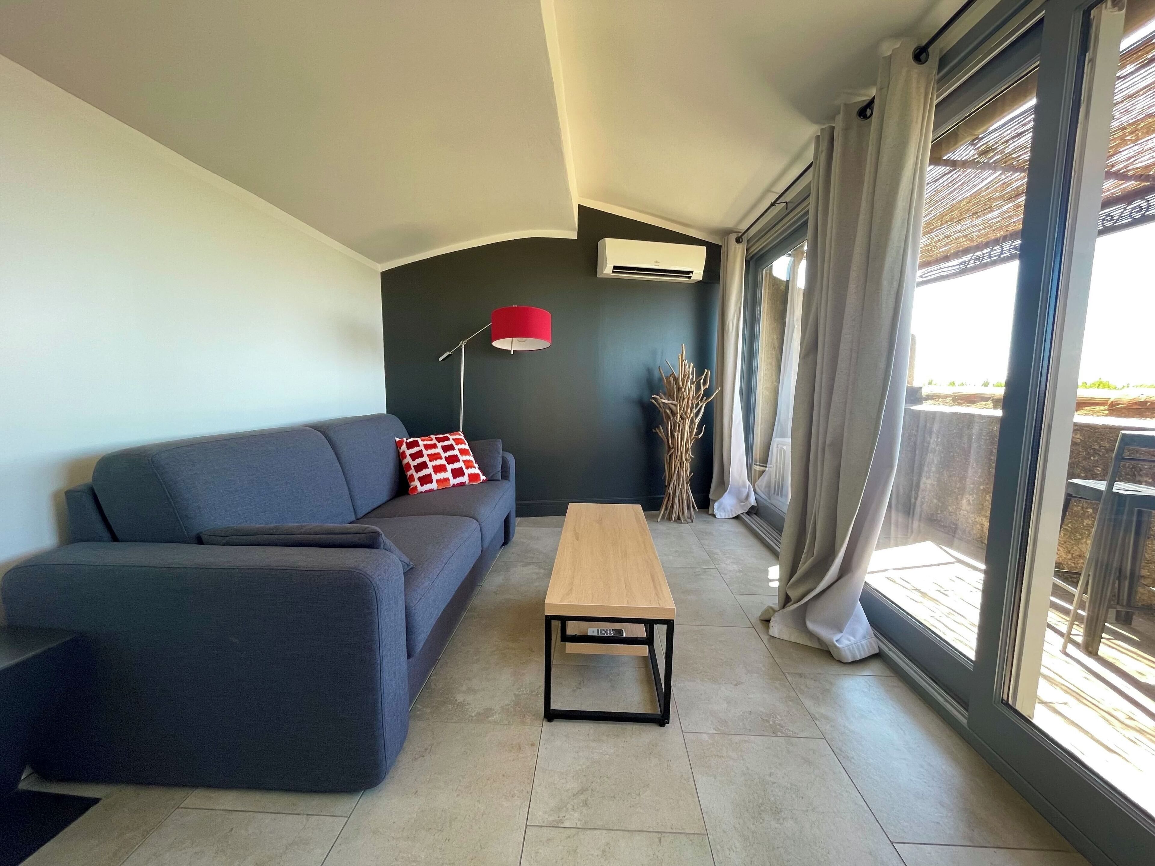 Een moderne woonkamer met een grijze bank, een houten salontafel en een rode vloerlamp.