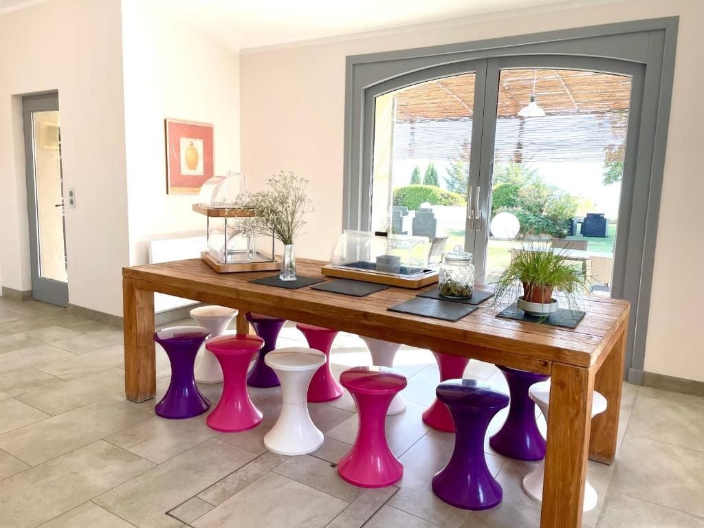A room with a wooden table, colorful stools, a window with a view, and a framed picture on the wall.