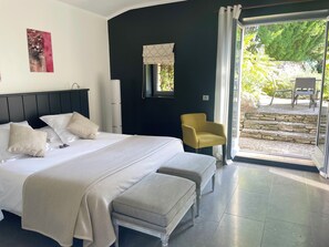 A bedroom with a large bed, a bench, a chair, and a view of the outdoors. - Domaine de l'Enclos (Gordes)