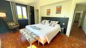A bedroom with a large bed, a bench, a chair, and a window.