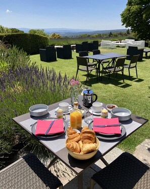 An outdoor dining area with a table set for breakfast, including croissants, a bottle of orange juice, and various breakfast items. - Domaine de l'Enclos (Gordes)