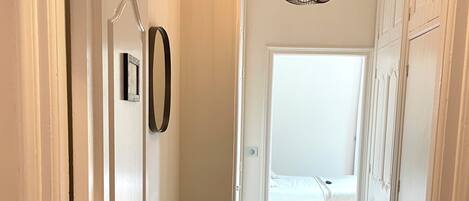 A hallway with a bench, a hanging light fixture, and a door leading to a bedroom.