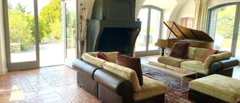 A spacious living room with a fireplace, sofas, and a piano.