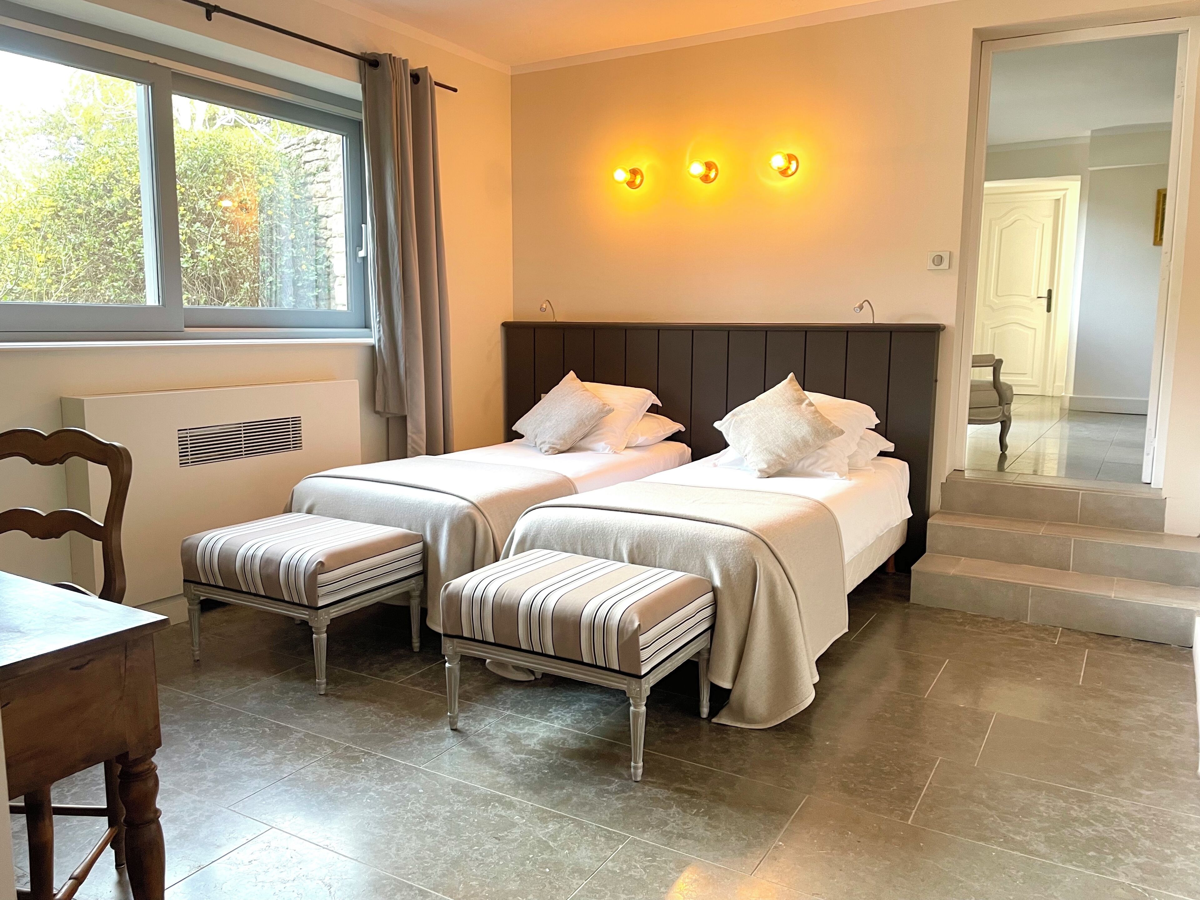 A bedroom with two beds, a window with curtains, a radiator, and a staircase leading to another room.
