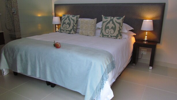 A neatly made bed with a floral centerpiece, two bedside lamps, and a headboard with a patterned design. - The Suit Park @ Pentagon (Bloemfontein)