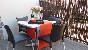 A table set with a bottle, glasses, and a bowl, surrounded by chairs, against a bamboo fence backdrop. - The Suit Park @ Pentagon (Bloemfontein)