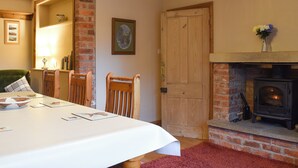 Un coin repas avec une table dressée pour quatre personnes, une cheminée et un fauteuil vert.