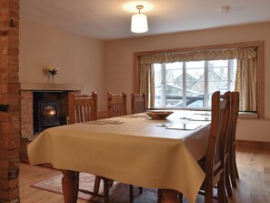 Una sala da pranzo con camino in mattoni, sedie di legno, un tavolo con tovaglia e una finestra con tende.