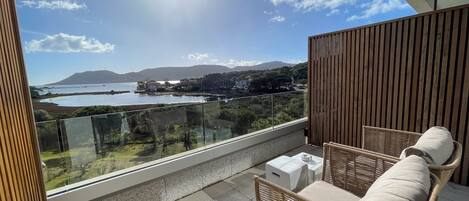 A balcony with wicker furniture, a clear view of a coastal landscape, and a mountain in the distance.