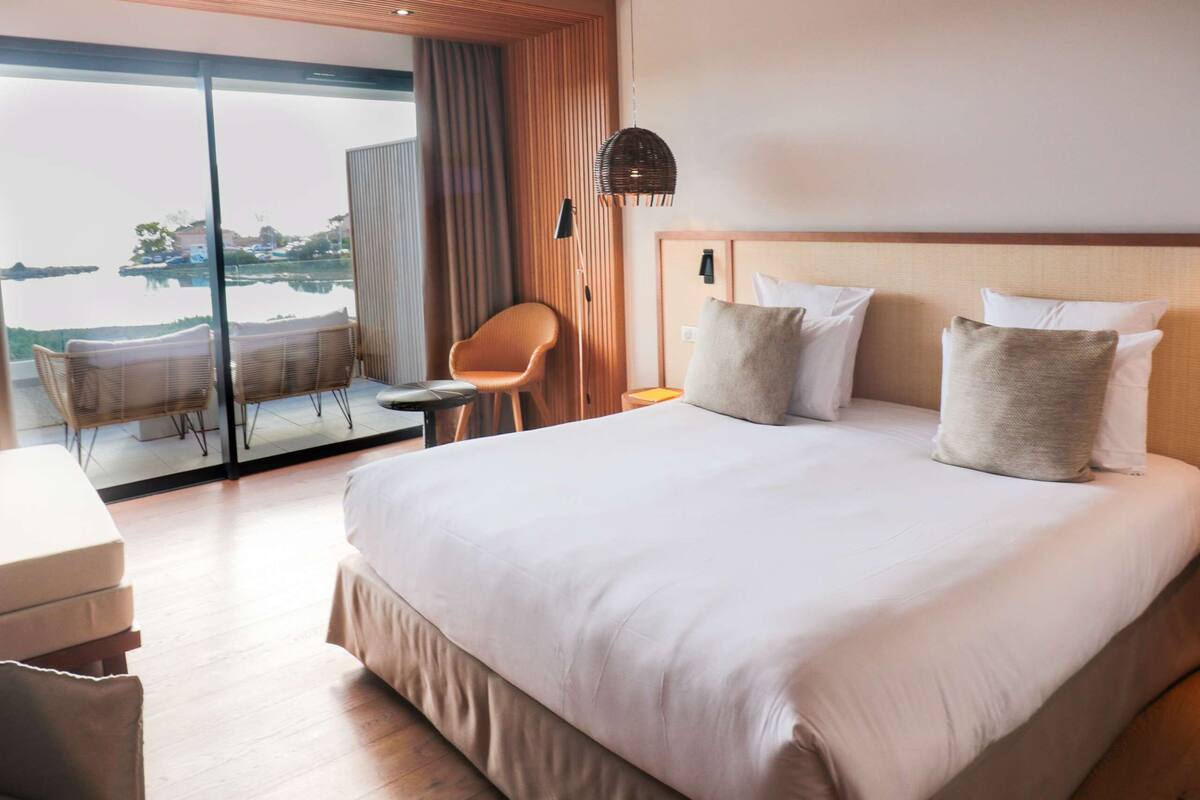 A modern hotel room with a large bed, a desk, and a view of the water.