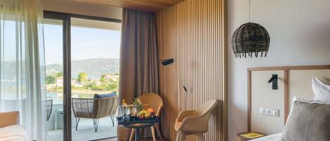 Quarto de hotel moderno com uma cama grande, uma mesa de jantar com frutas, duas cadeiras de vime e vista para o exterior, além de teto com ripas de madeira.