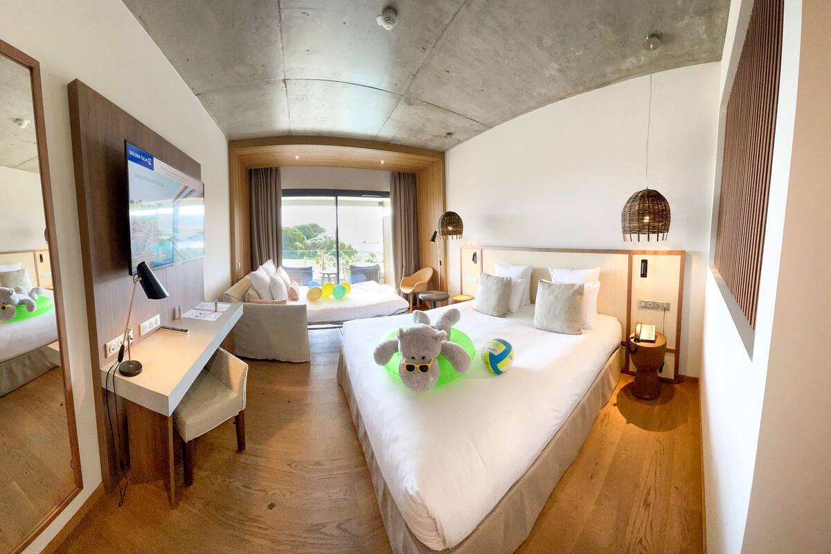 A hotel room with a bed, a desk, a chair, a TV, and a view of the outdoors.