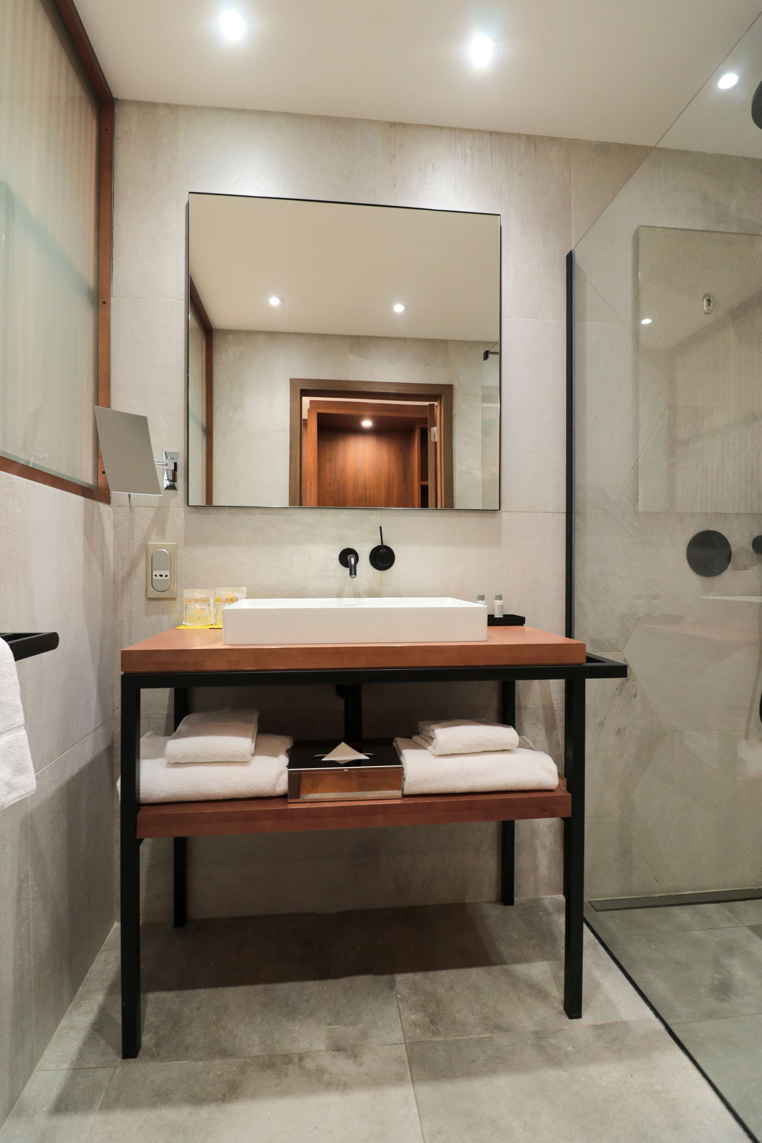 Une salle de bain moderne avec un meuble-lavabo en bois, un grand miroir et une cabine de douche en verre.