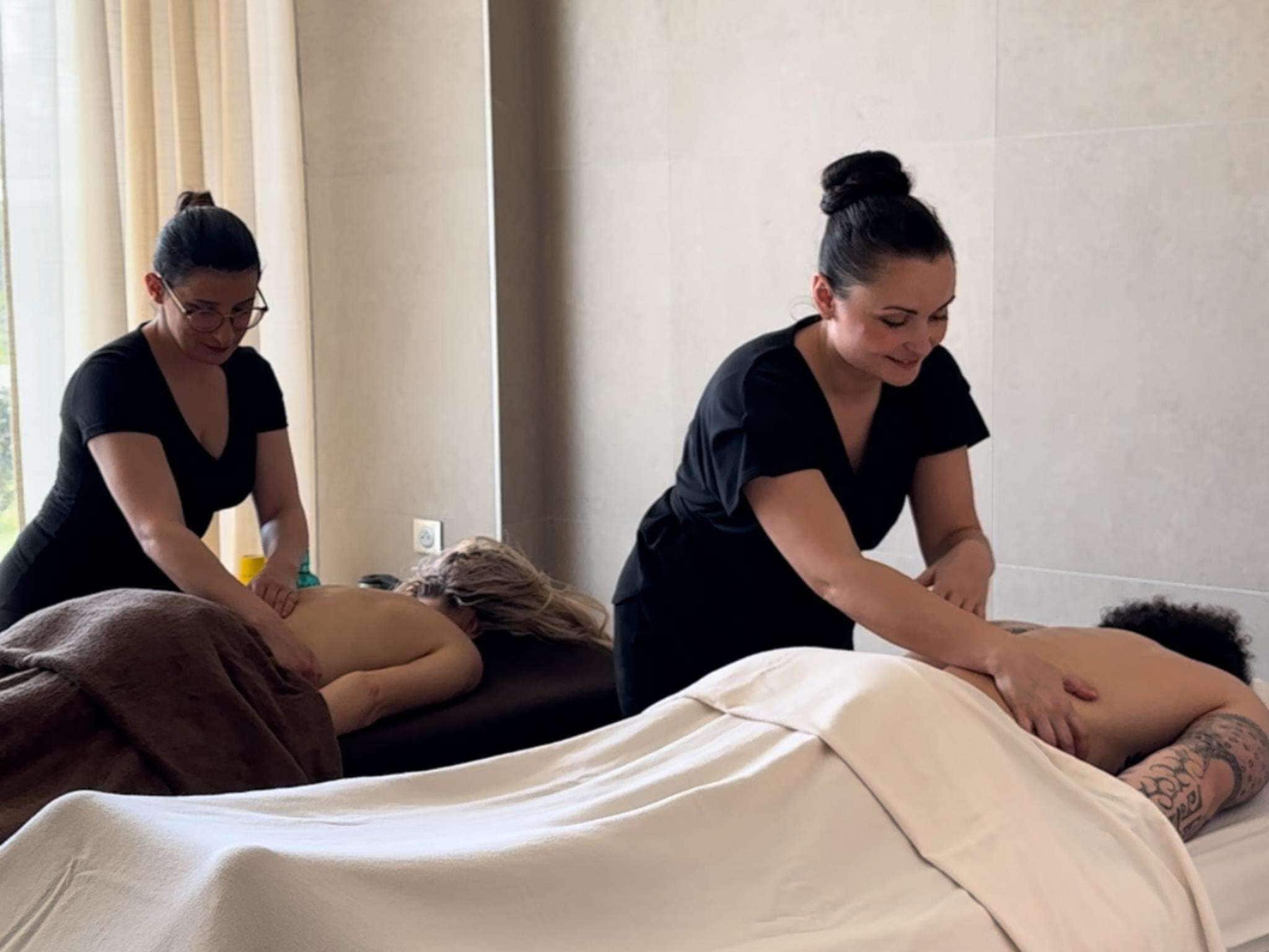 A massage therapy room with two therapists attending to a client on a massage table.