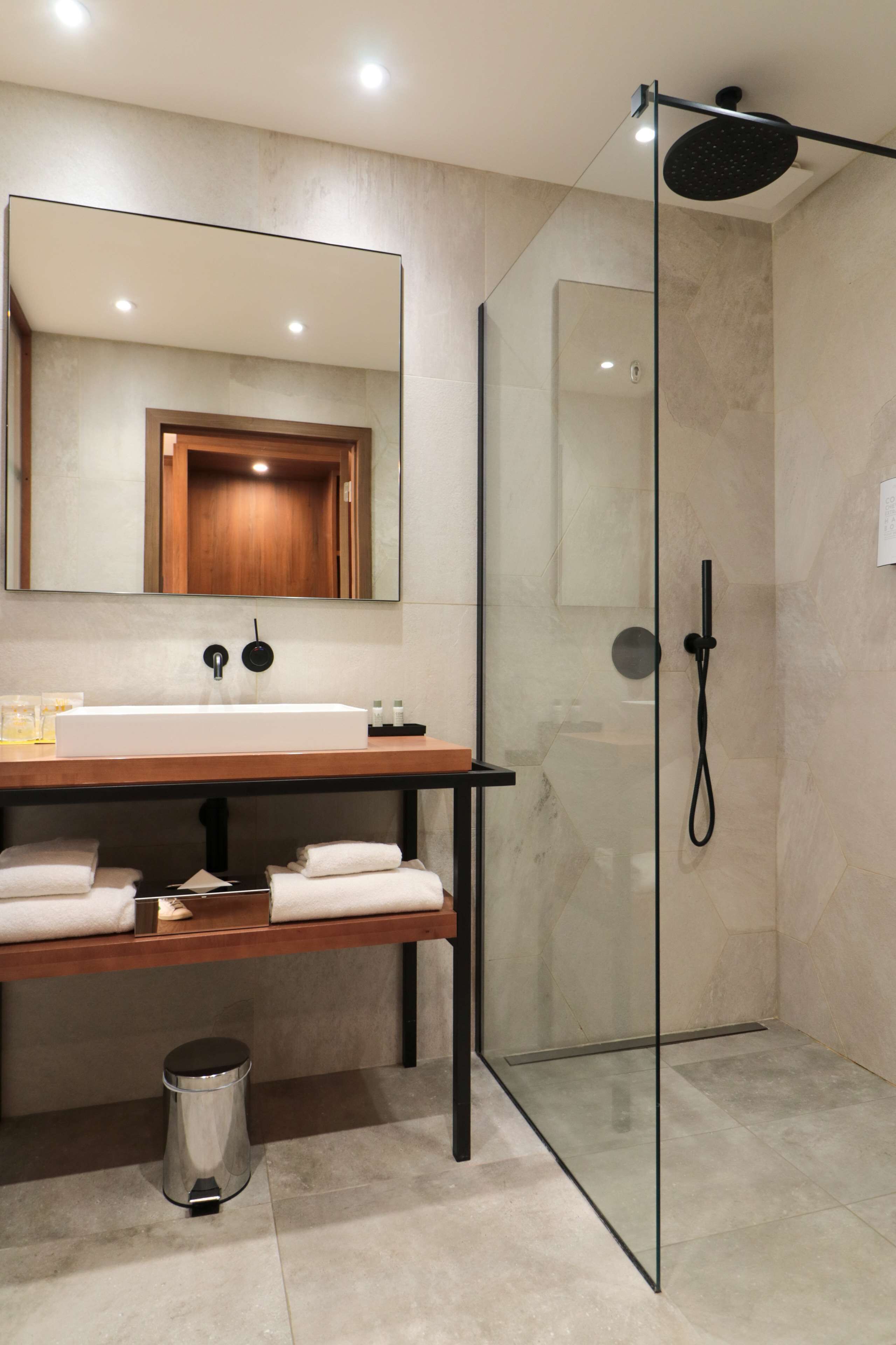 Un baño moderno con ducha de vidrio, tocador de madera y un espejo grande.