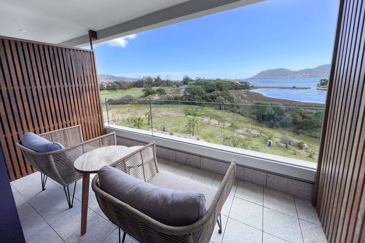 A balcony with wicker furniture, a view of a coastal landscape, and a clear sky.