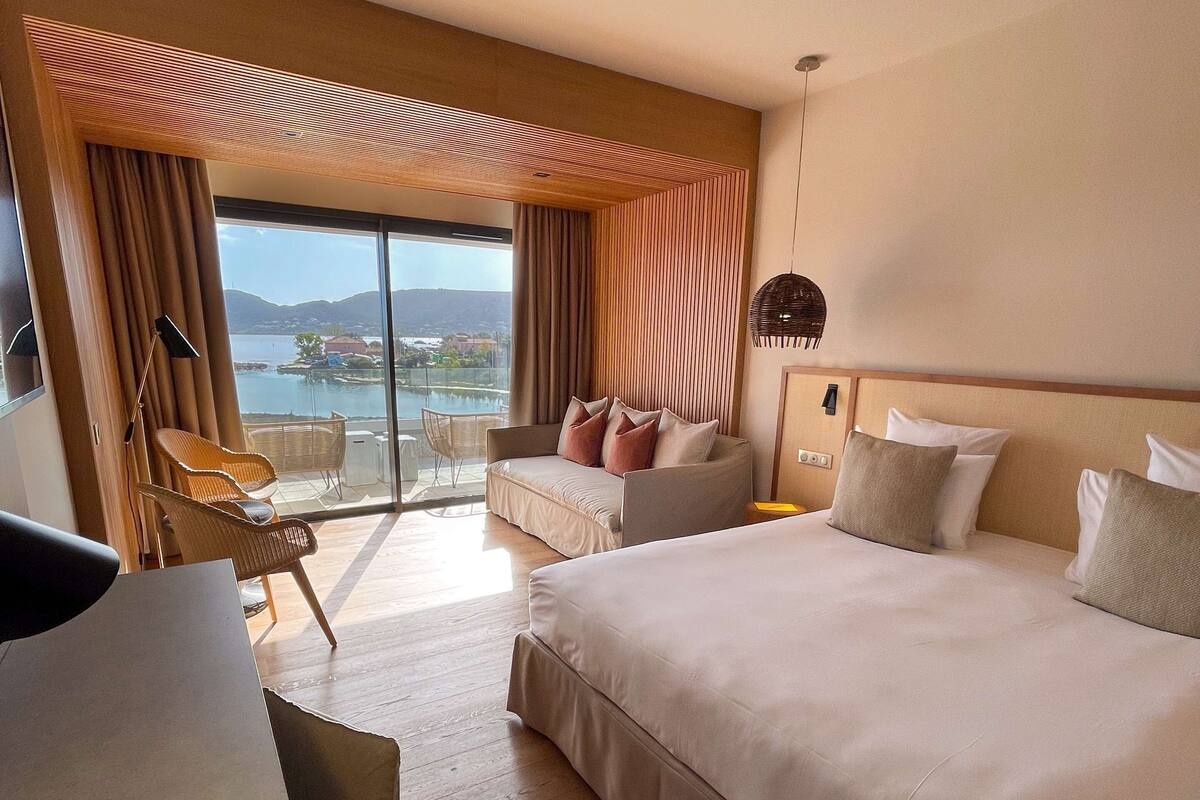 A hotel room with a large bed, a desk, a chair, and a view of a body of water.