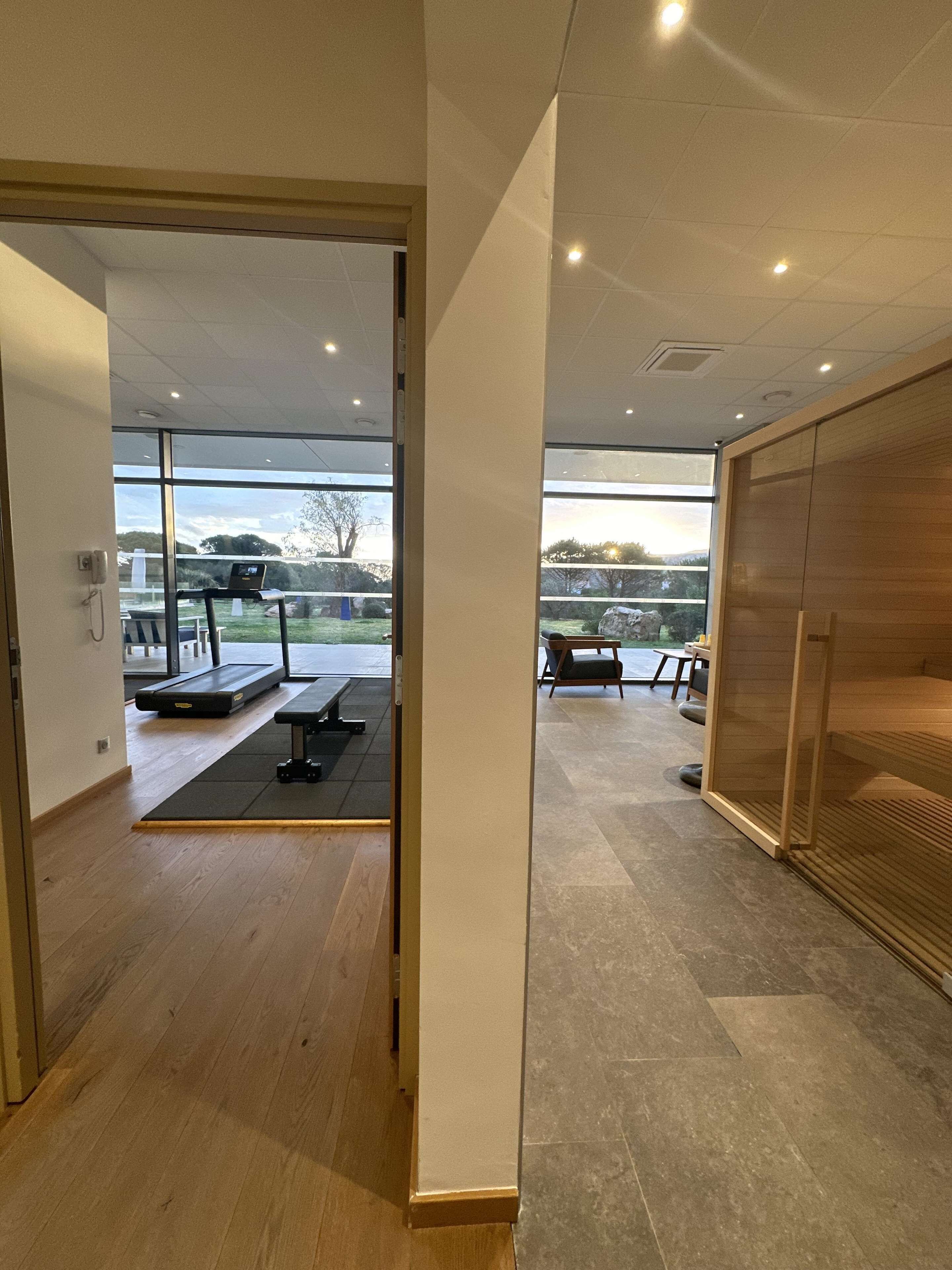 A modern interior with a wooden floor, a treadmill, and a view of the outdoors through large windows.