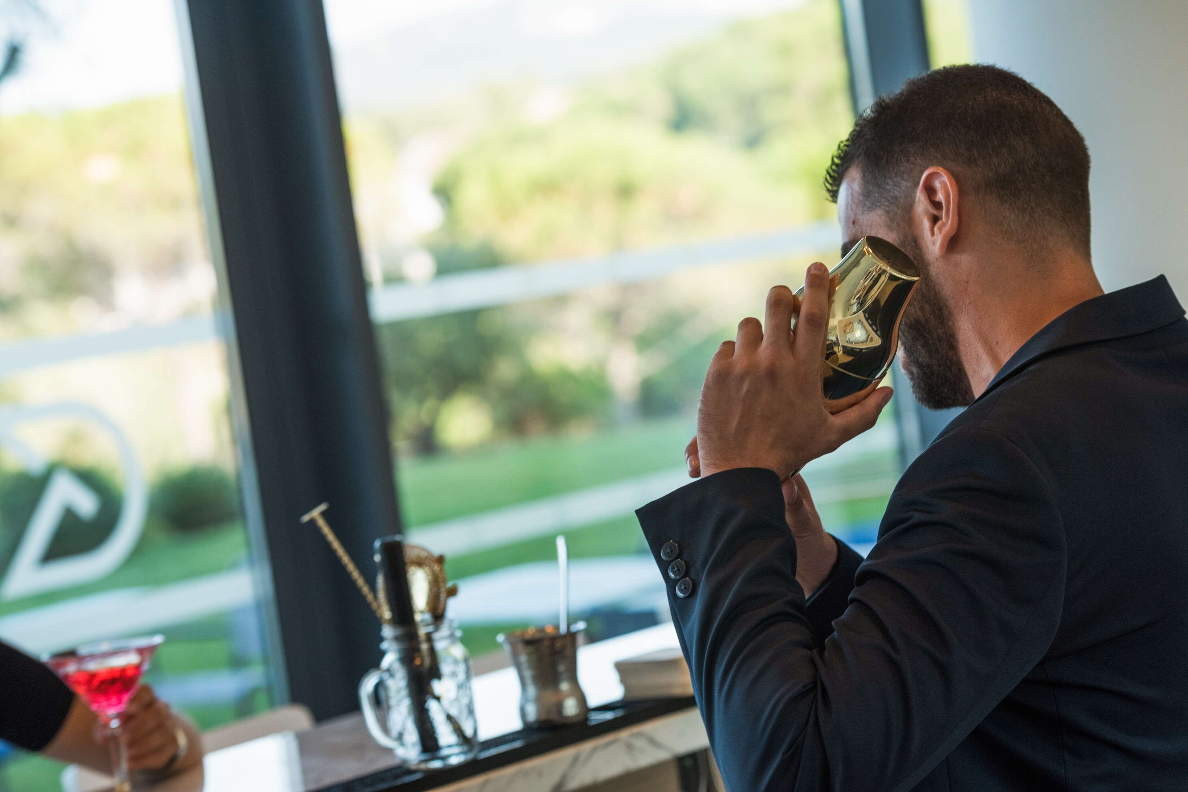 A person in a dark suit drinking from a glass.