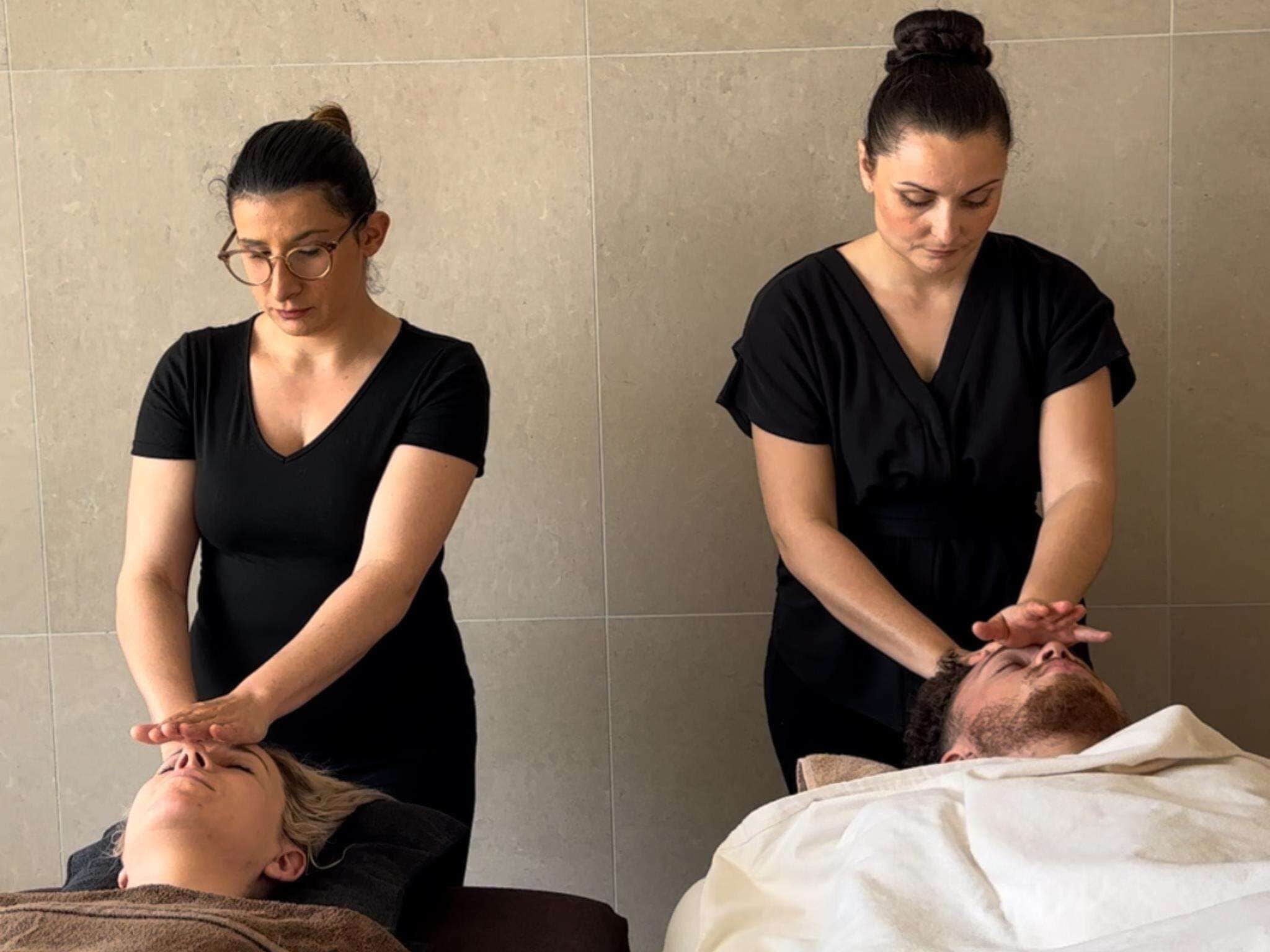 A massage therapy session in a room with tiled walls and a plain backdrop.