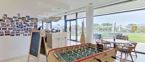 A modern indoor space with a foosball table, a wall of photographs, and a view of the outdoors.