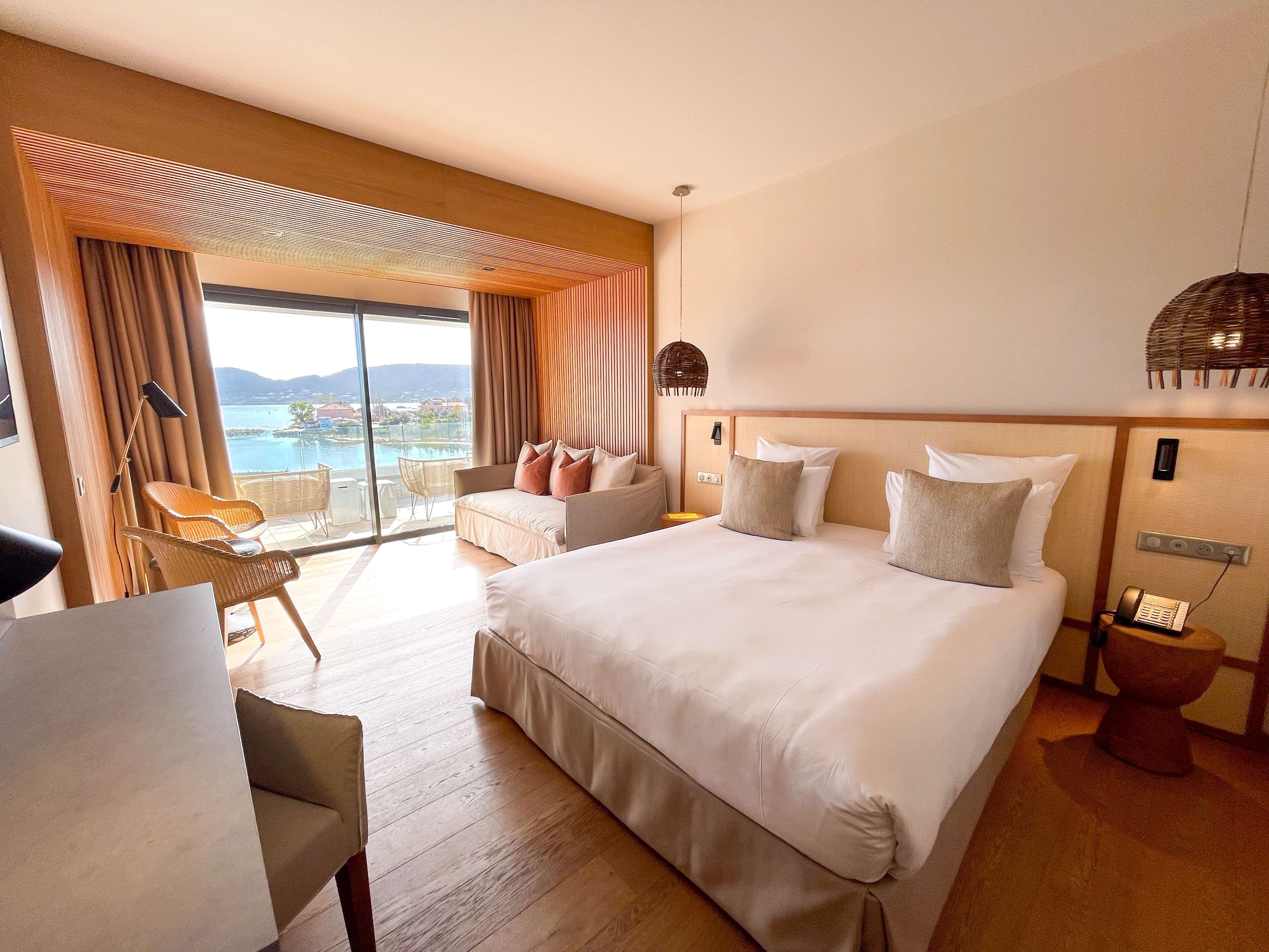Un'ampia camera da letto con un letto grande, un'area salotto con poltrone, vista sull'esterno e un balcone.