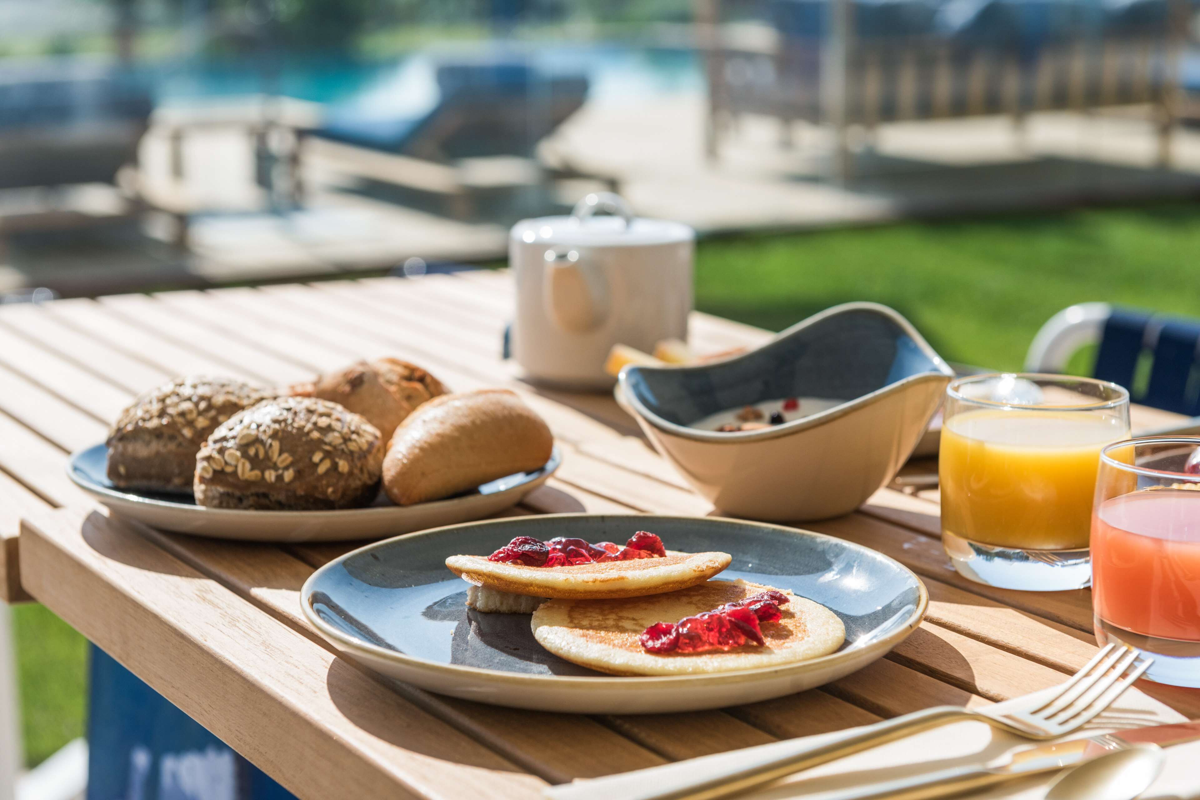 Una mesa de desayuno con pasteles, un tetera, un tazón de cereal y vasos de jugo de naranja y una bebida rosada.