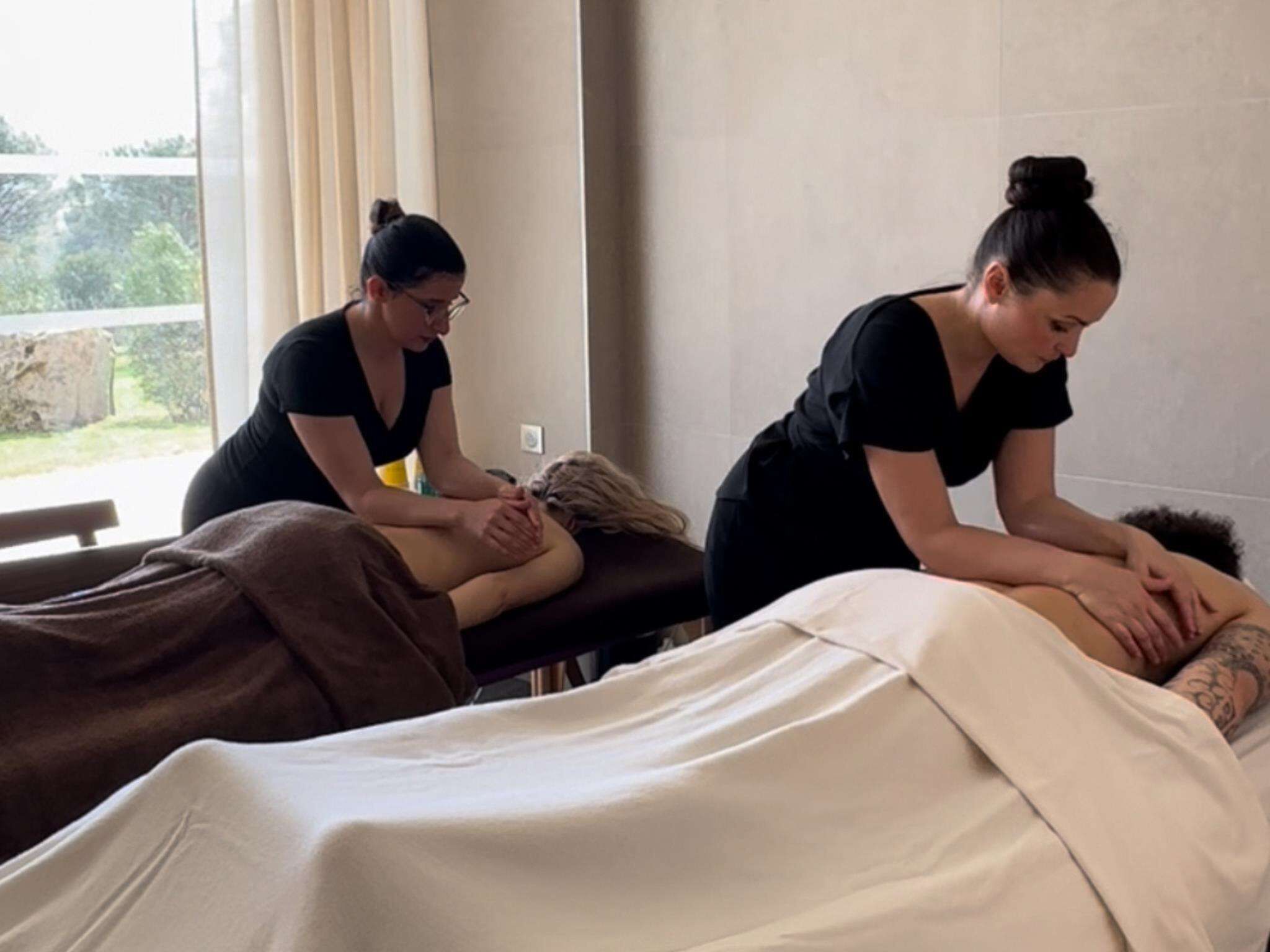 Un cuarto de terapia de masajes con dos clientes recibiendo masajes en la espalda.