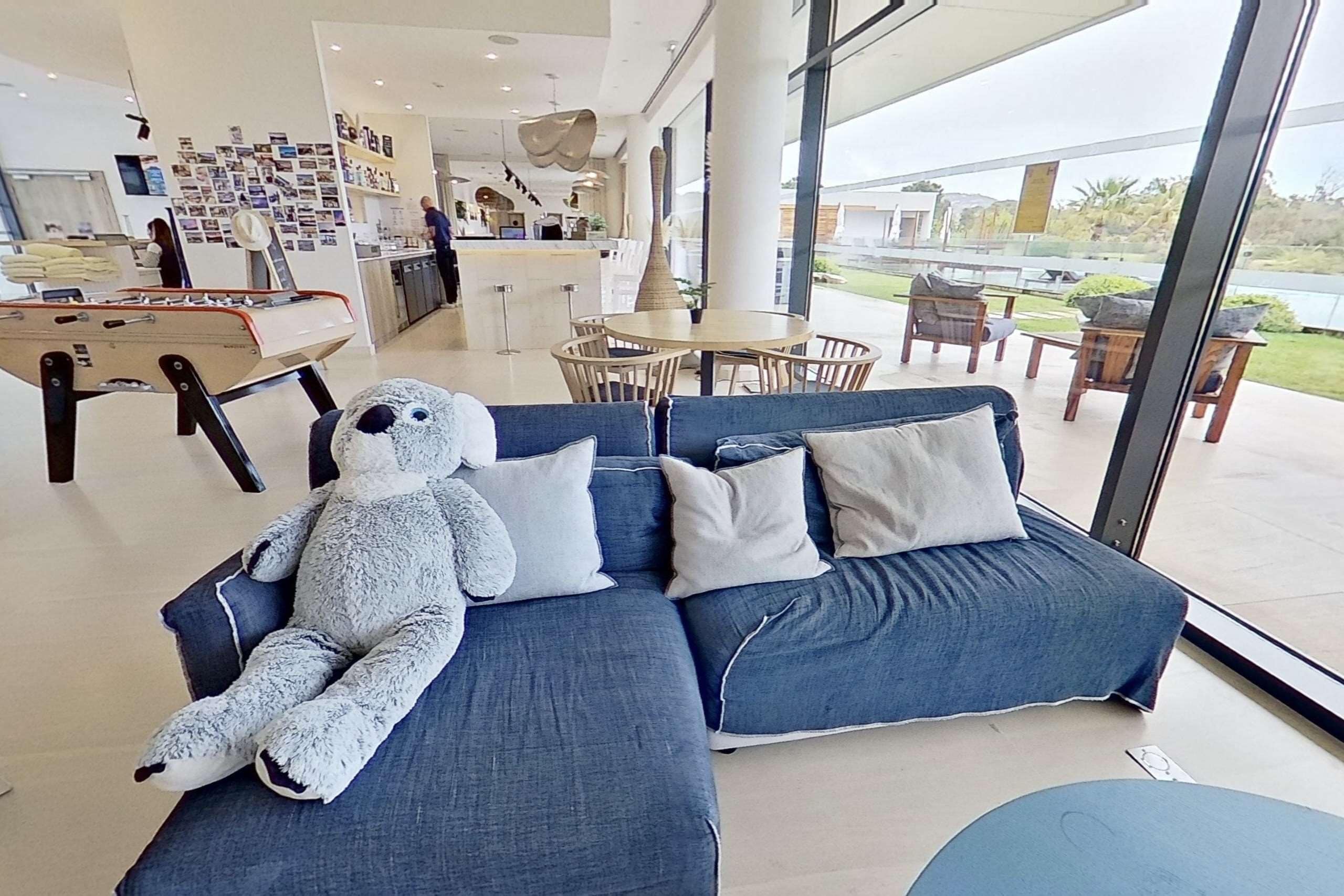 Un moderno vestíbulo de hotel con mesa de billar, un peluche grande y un sofá con cojines.