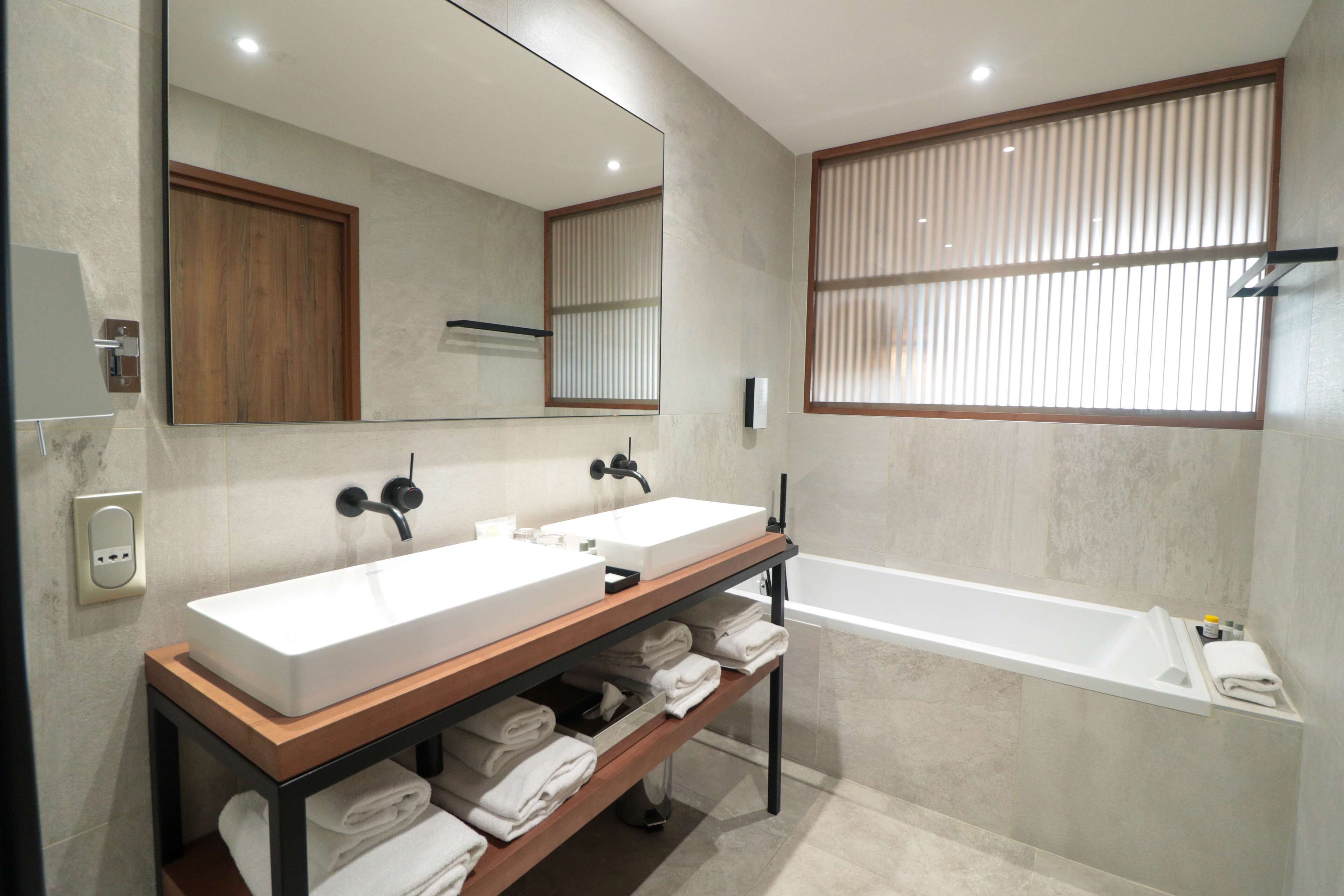 Une salle de bain moderne avec deux vasques, un grand miroir, un meuble-lavabo en bois et une baignoire.